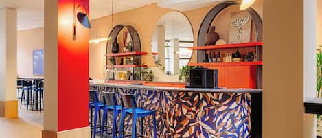 A modern bar area with a colorful abstract wall design, red shelving, and blue bar stools.