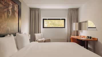 Une chambre d’hôtel avec un grand lit, un bureau avec une chaise, une fenêtre avec des rideaux et un tableau au mur.