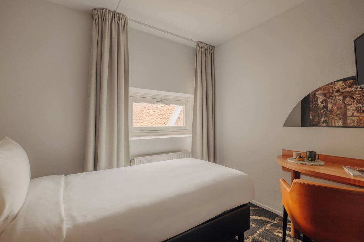 Une chambre d’hôtel avec un lit, un bureau et une fenêtre avec des rideaux.
