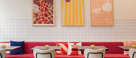 A restaurant with a red booth seating area, white tiled backsplash, and framed artwork on the wall.
