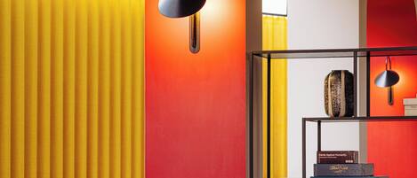 A modern interior with a red accent wall, a yellow curtain, a black hanging lamp, a wooden chair, and a table with books.