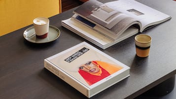 A yellow sofa with a red and white pillow, a coffee cup, a book, and a magazine on a dark table.