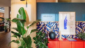 Un mostrador de recepción con un cartel que dice 'RECEPTION', una obra de arte enmarco, un florero negro y plantas en macetas.