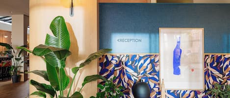 En receptionsdisk med en skylt som visar ordet ”RECEPTION”, ett inramat konstverk, en svart vas och krukväxter.