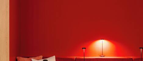Un rincón acogedor con un banco tapizado rojo, una mesita con un libro y una lámpara, y una pared de madera.