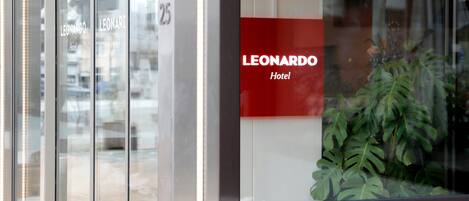 Entrada de un hotel con puerta de cristal y un letrero rojo que dice "LEONARDO Hotel".
