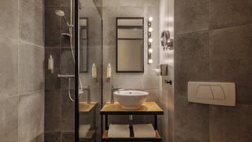 Un baño moderno con ducha envuelta en vidrio, tocador con lavabo y espejo con iluminación.