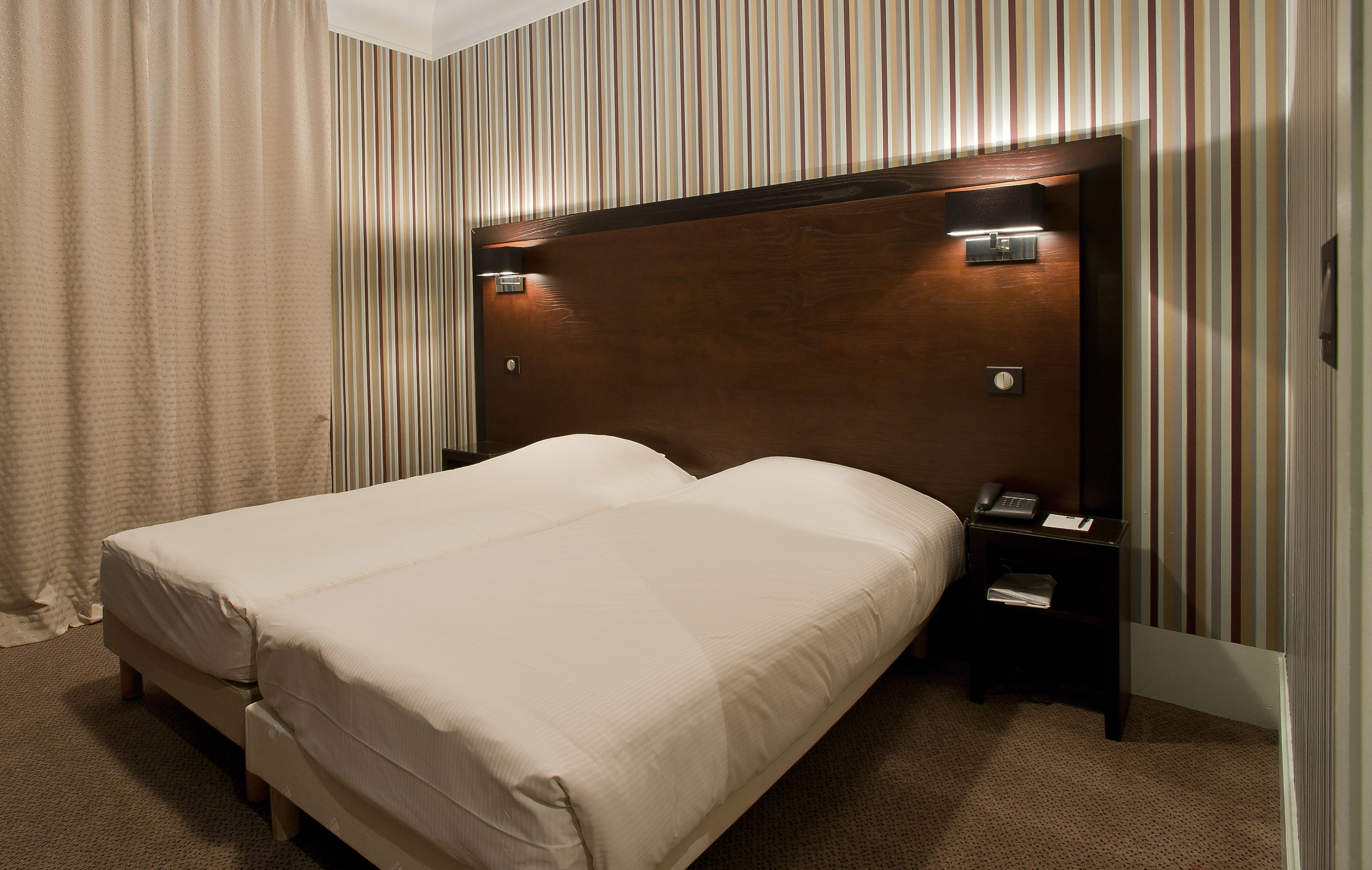 A hotel room with a large bed, a wooden headboard, a nightstand with a phone, and striped wallpaper.