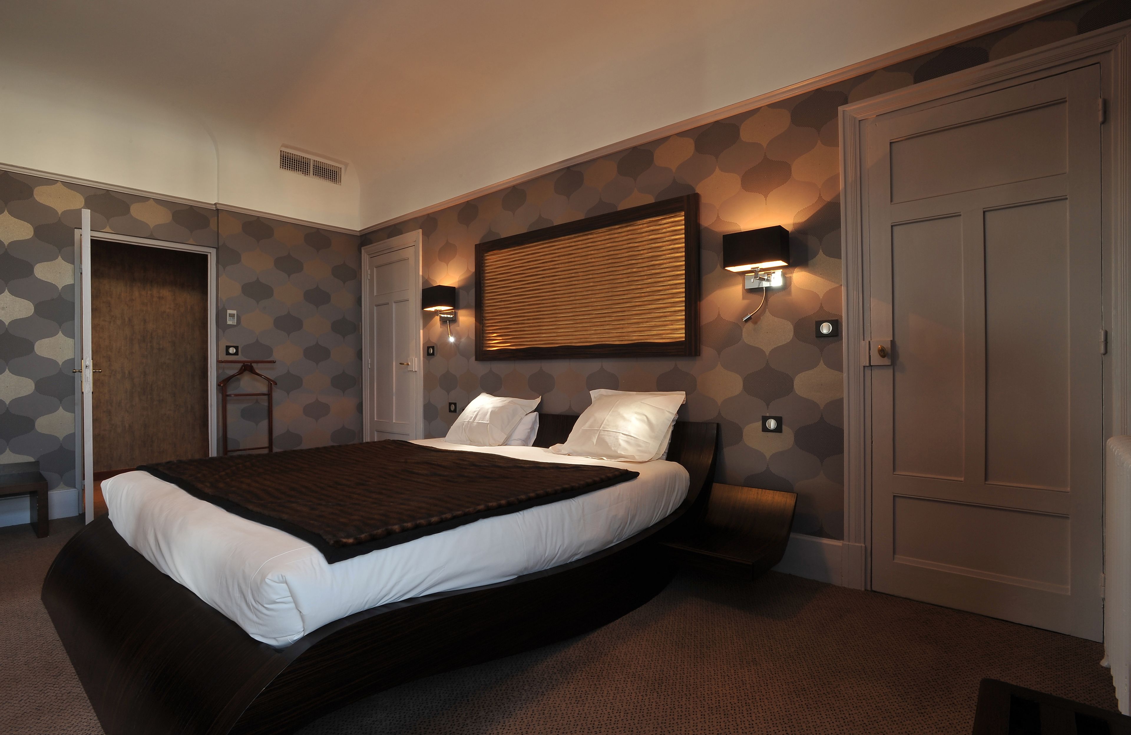 A bedroom with a large bed, two bedside tables, a wall-mounted light, and a door.