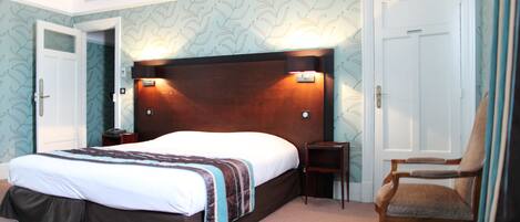 A hotel room with a large bed, two bedside tables, a wooden headboard, a chair, and patterned wallpaper.