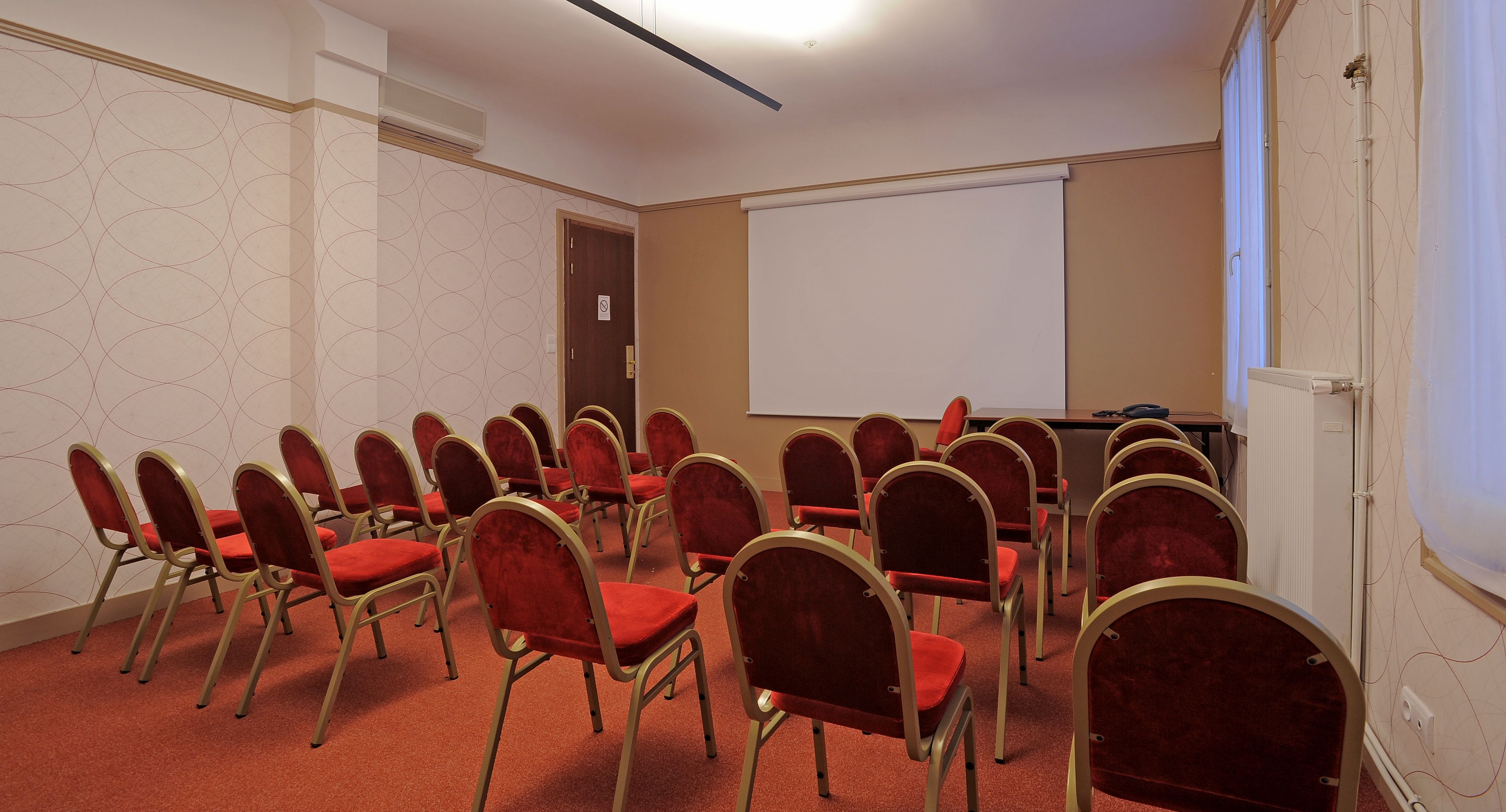 A conference room with rows of red chairs, a whiteboard, and a projector screen.
