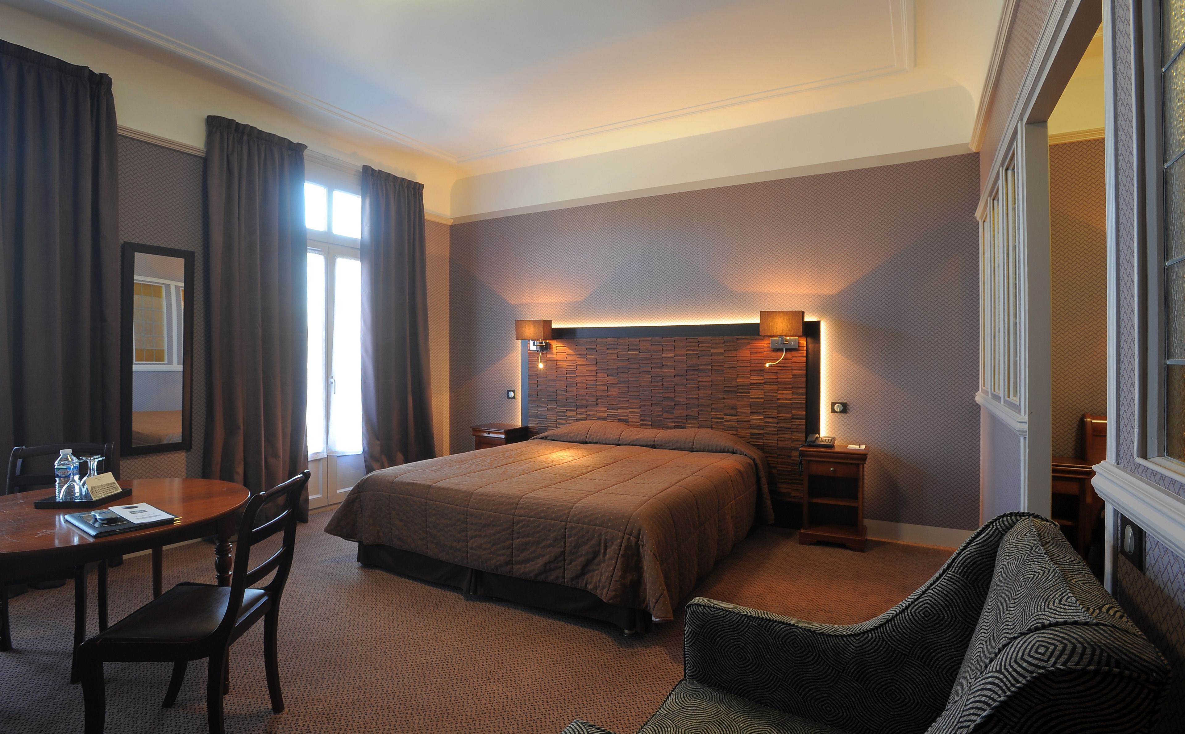 A hotel room with a large bed, a desk with a chair, a sofa, and a mirror.