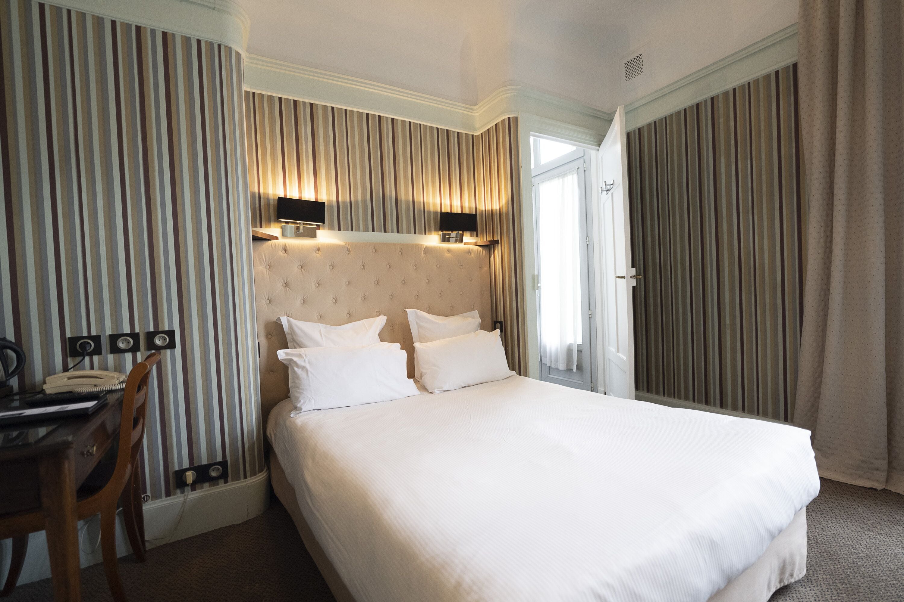Habitación de hotel con una cama grande, un escritorio con una silla y una ventana con cortinas.