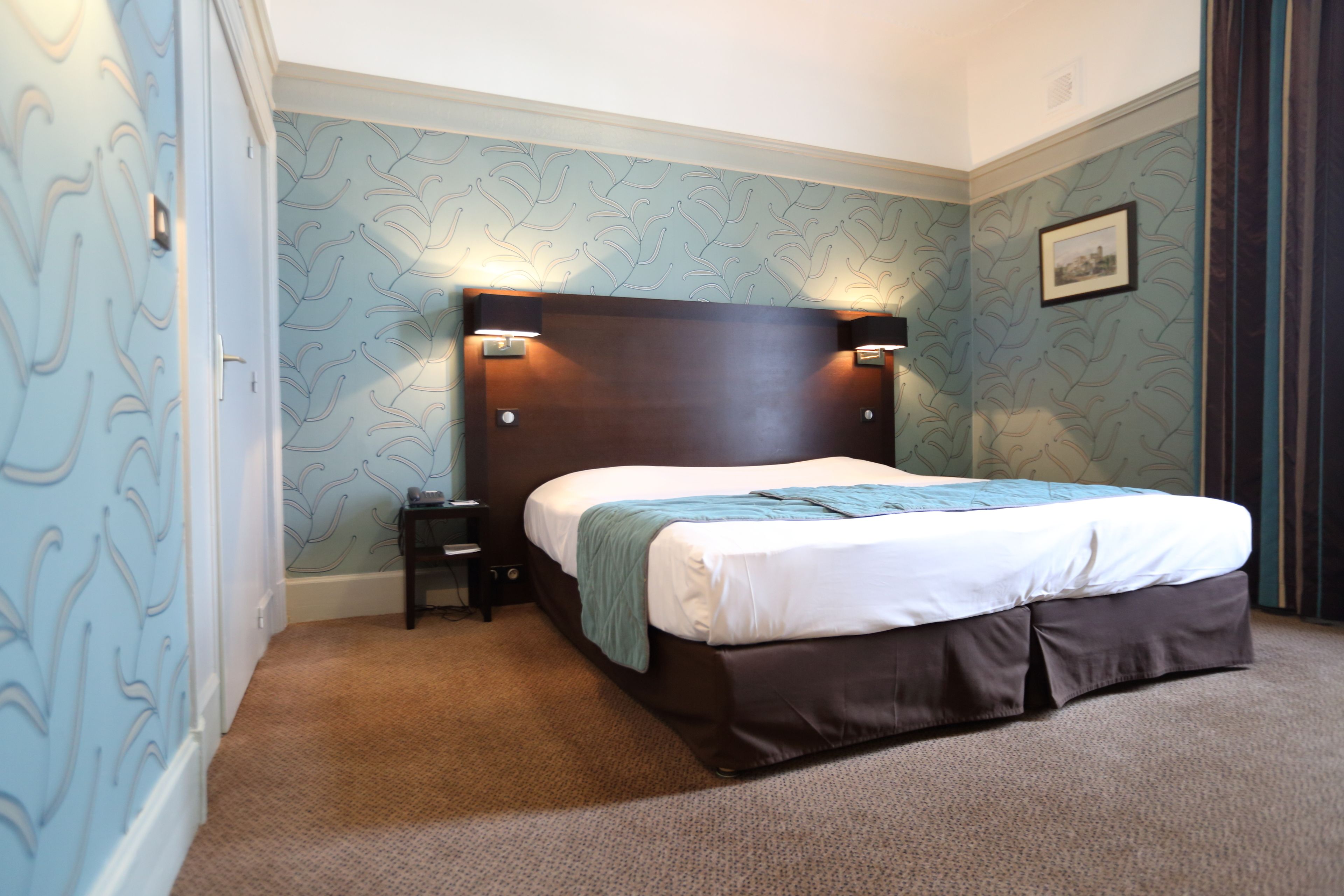 A bedroom with a large bed, two bedside lamps, a nightstand, and a picture on the wall.