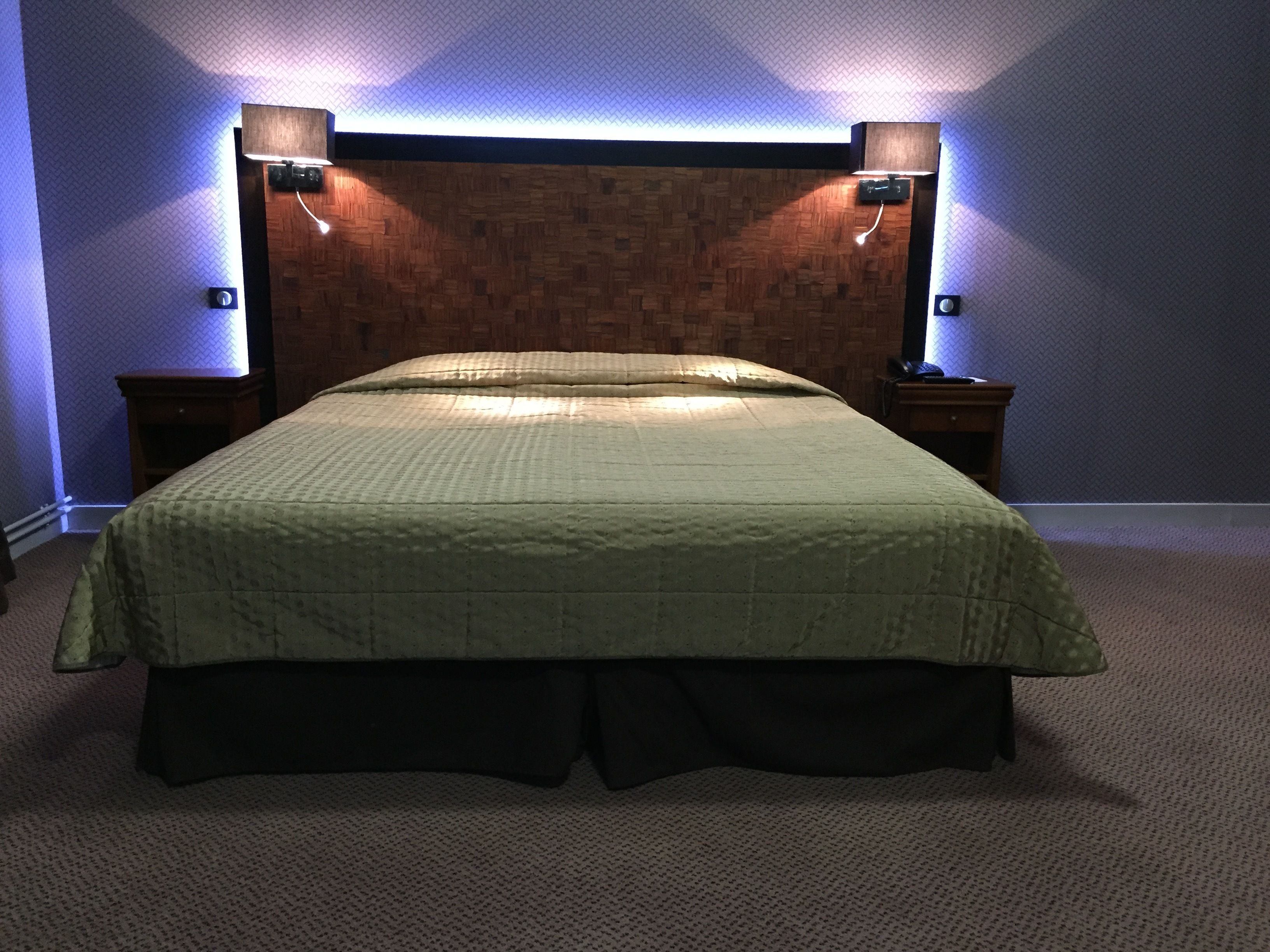 Een slaapkamer met een houten hoofdeinde, twee bedlampen, een groene sprei en een vloerbedekking.