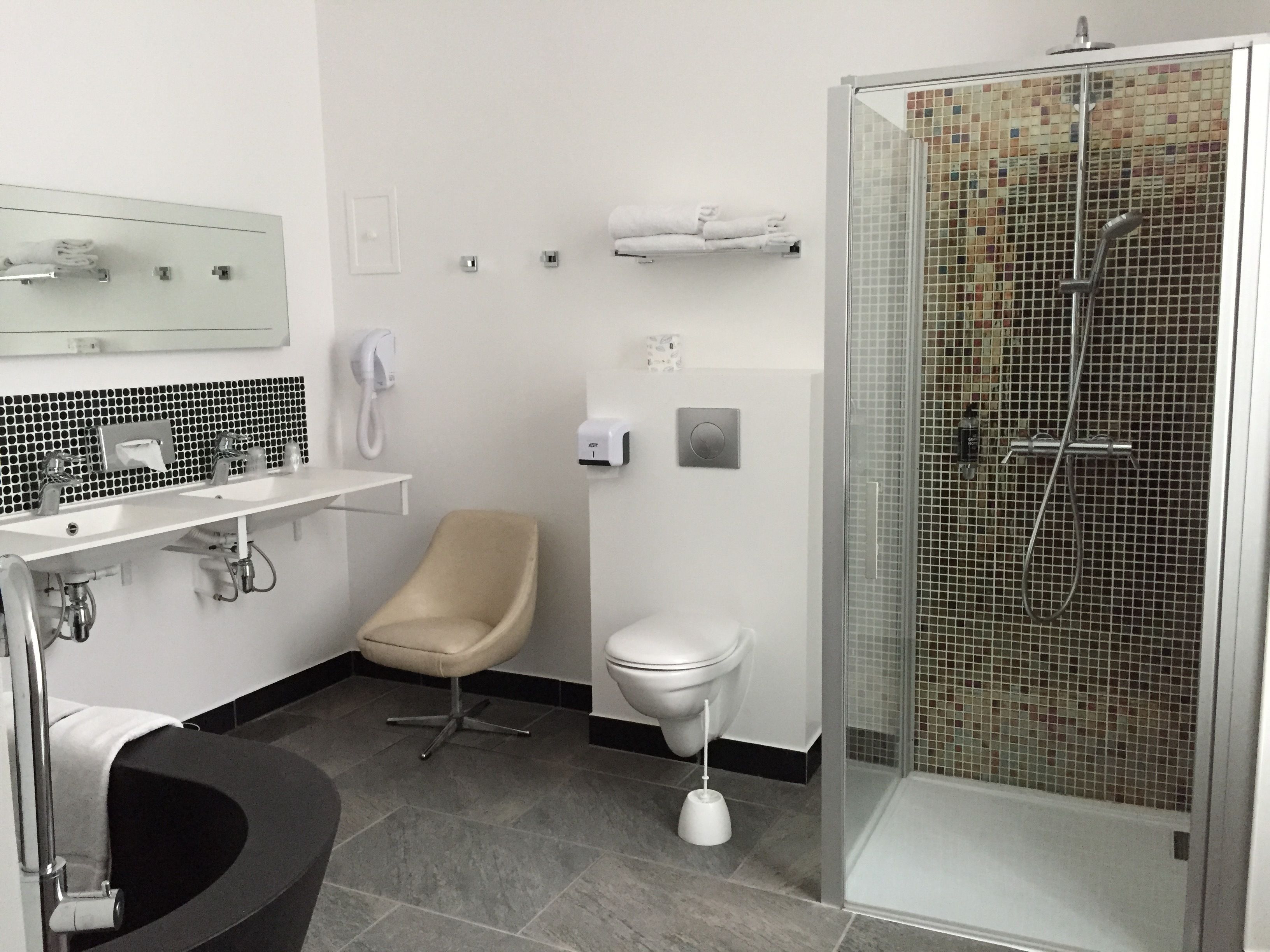 Un bany modern amb dutxa de vidre, vàter, un lavabo amb mirall i una cadira.