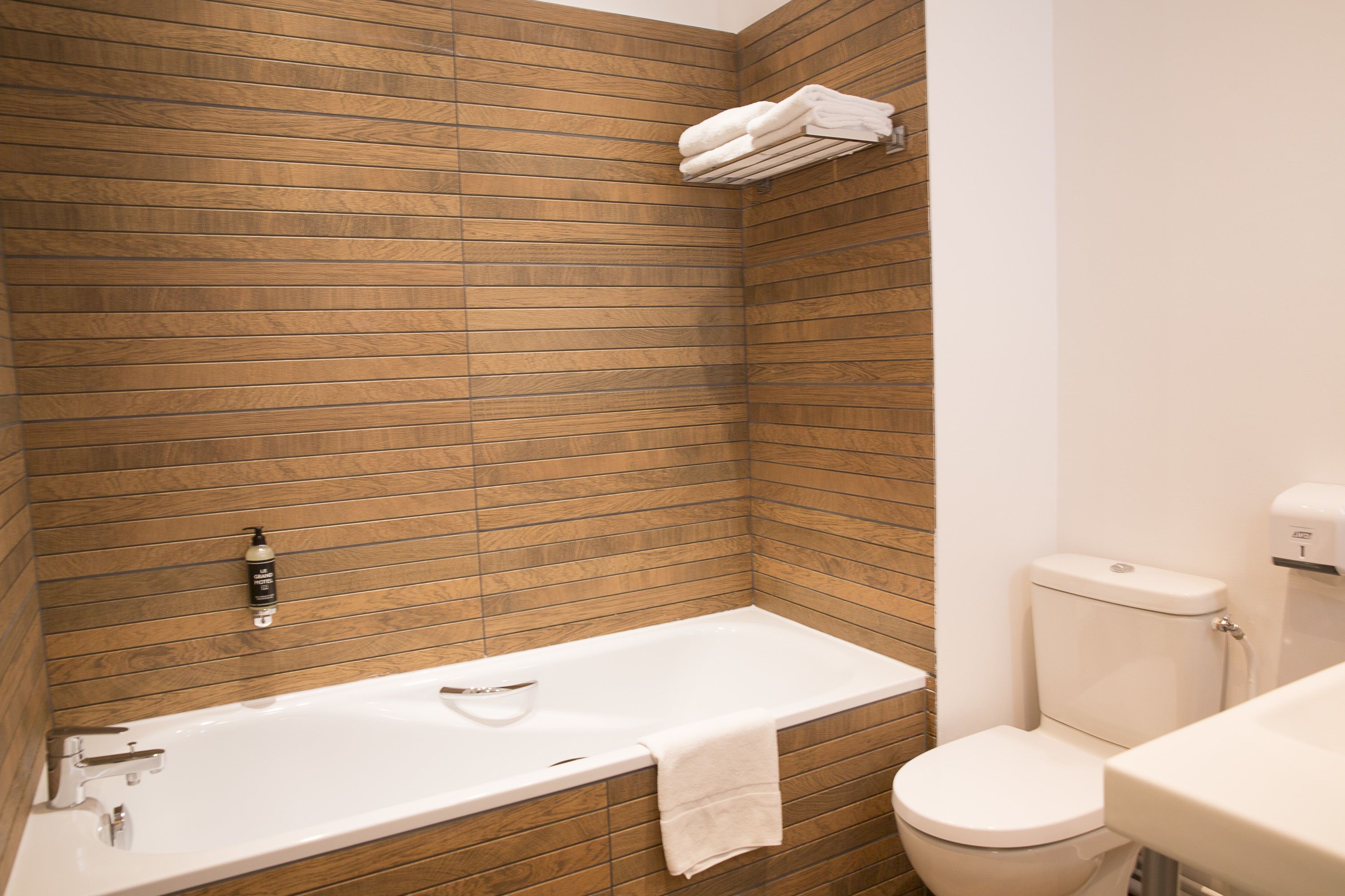 Een badkamer met een houten wand, een witte badkuip, een toilet en een wastafel.