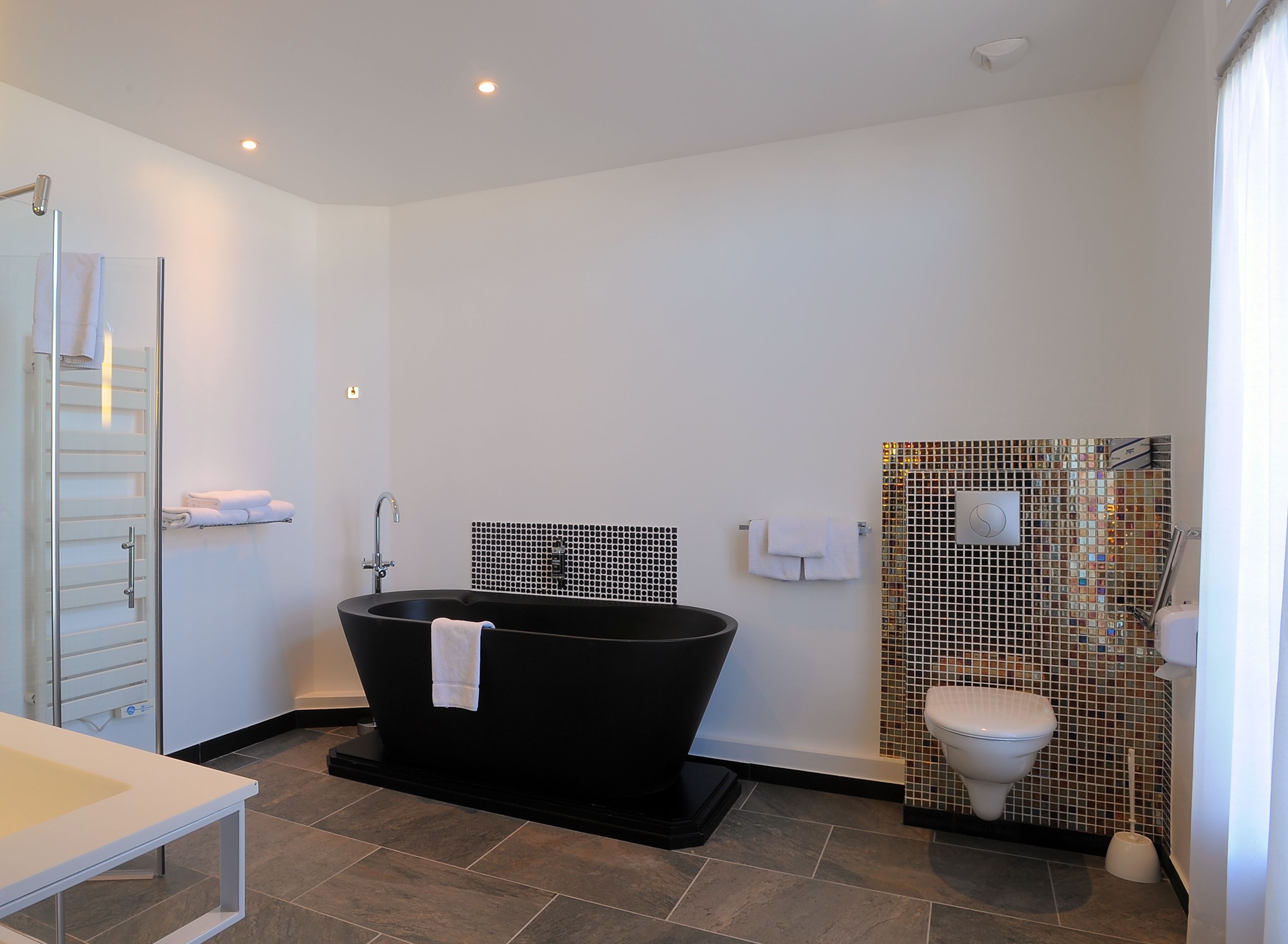 Een moderne badkamer met een vrijstaand bad, een toilet met een mozaïektegel decoratie en een douchecabine van glas.