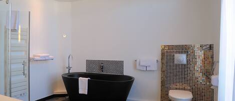 Een moderne badkamer met een vrijstaand bad, een toilet met een mozaïektegel decoratie en een douchecabine van glas.