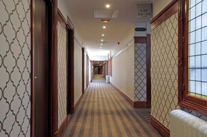 Pasillo de hotel con paredes estampadas, alfombra a rayas y un cartel que indica la ubicación del ascensor.