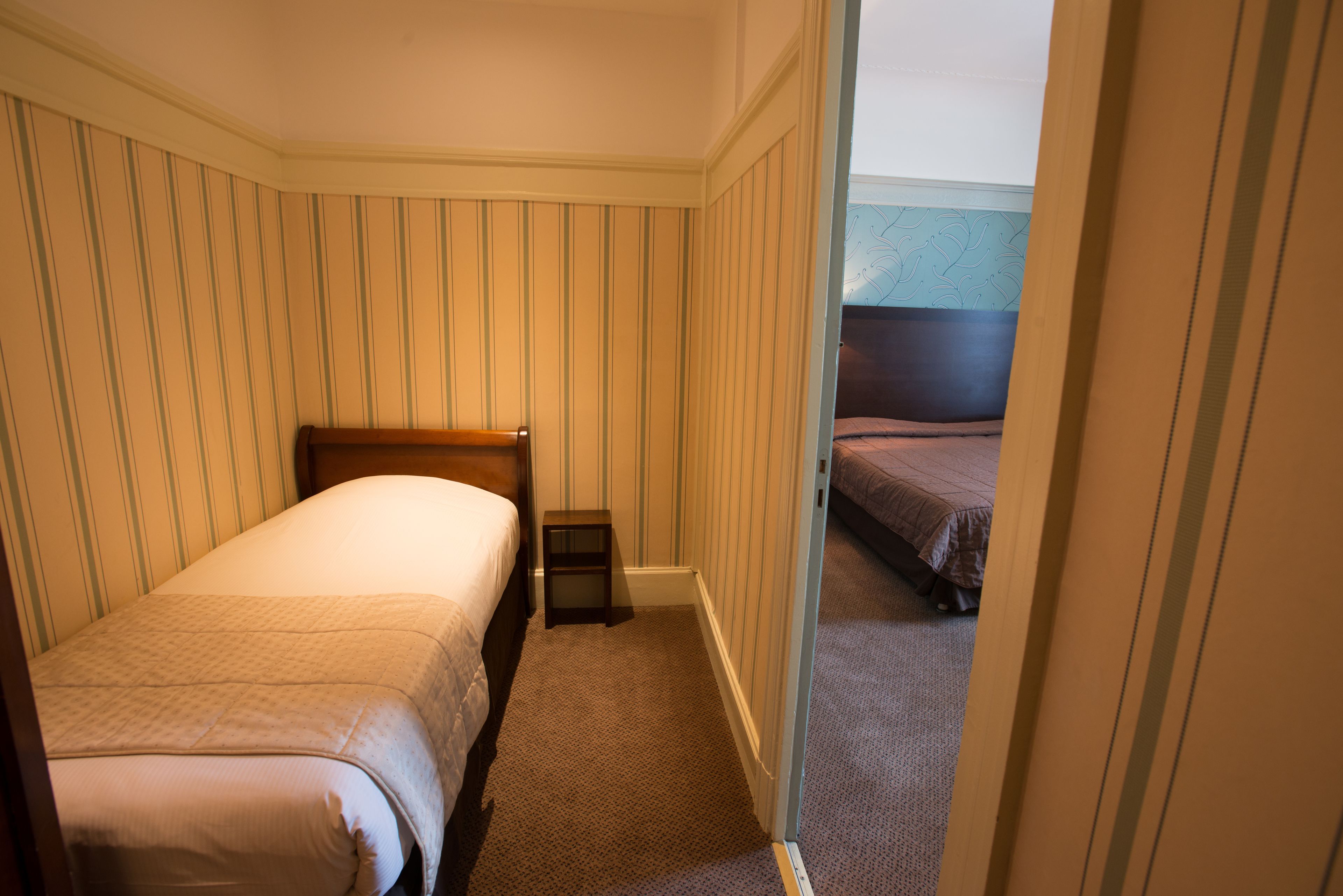 Quarto de hotel com duas camas de solteiro, uma pequena mesa de cabeceira e piso coberto de carpete.