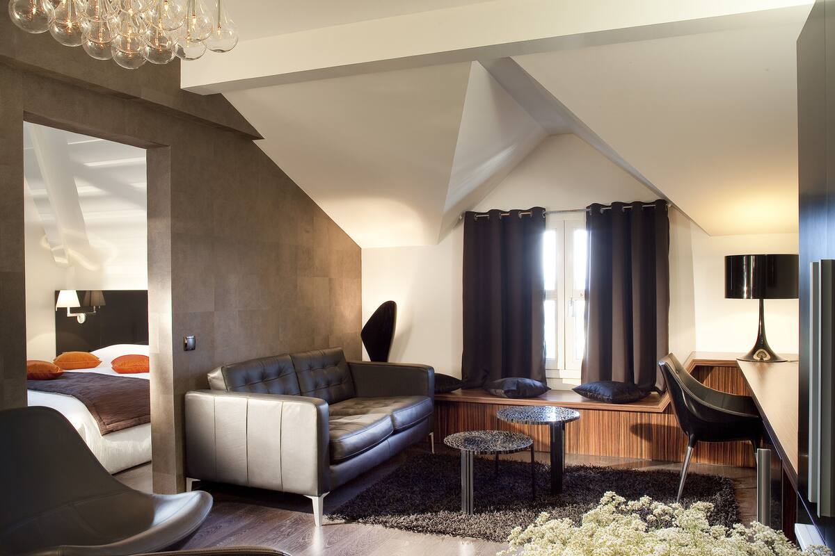 Ein modernes Schlafzimmer im Loft-Stil mit schrägem Dach, einem großen Bett, einer Couch, einem Essbereich und Blick ins Freie.