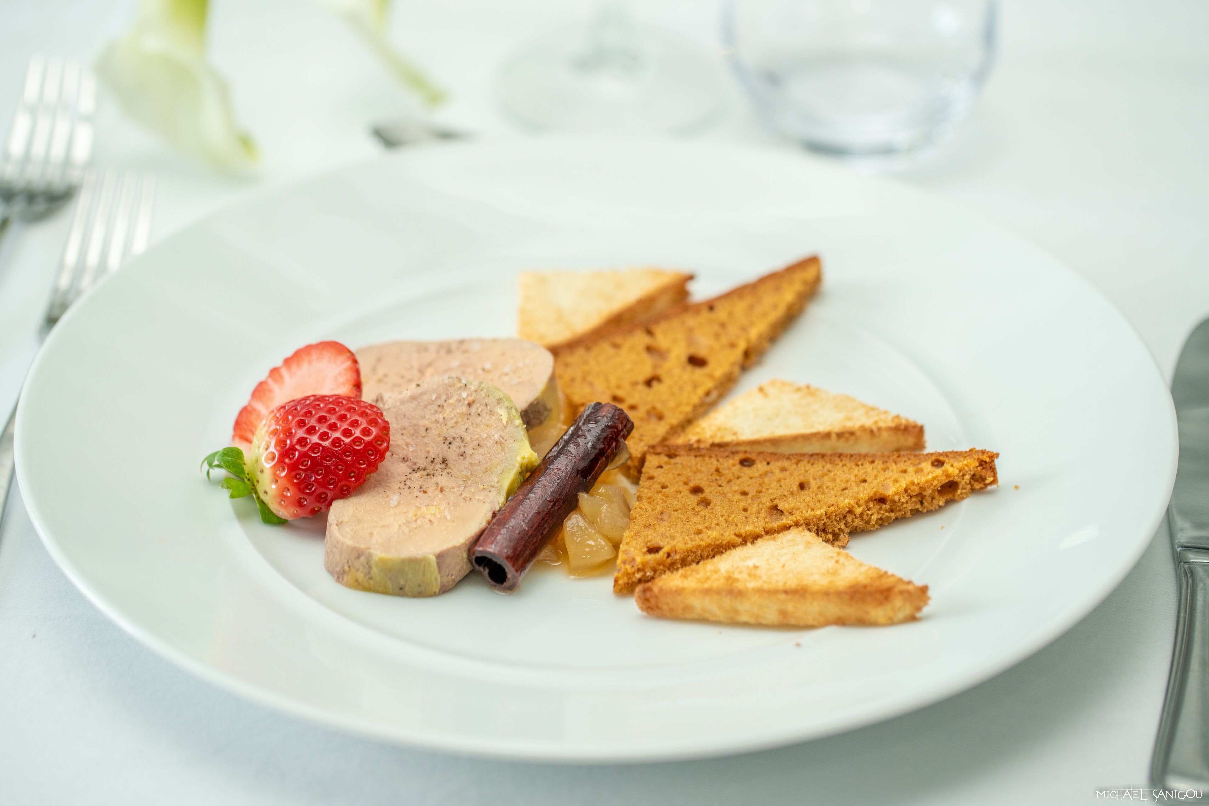 A plate with toast, a slice of meatloaf, a strawberry, and a cinnamon stick.