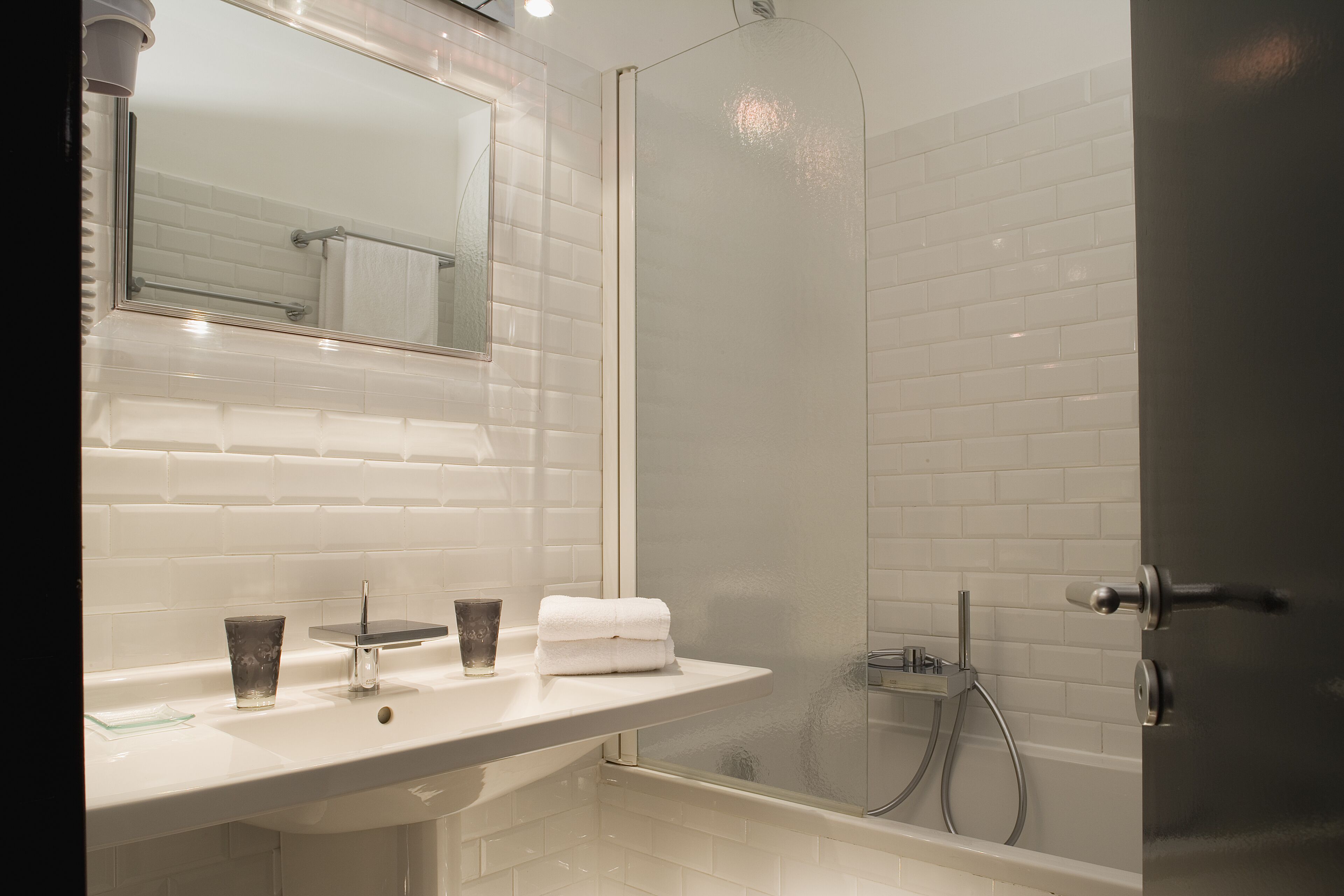 Une salle de bain moderne avec une douche carrelée de carreaux blancs, une porte de douche en verre et un lavabo blanc avec un verre à côté.