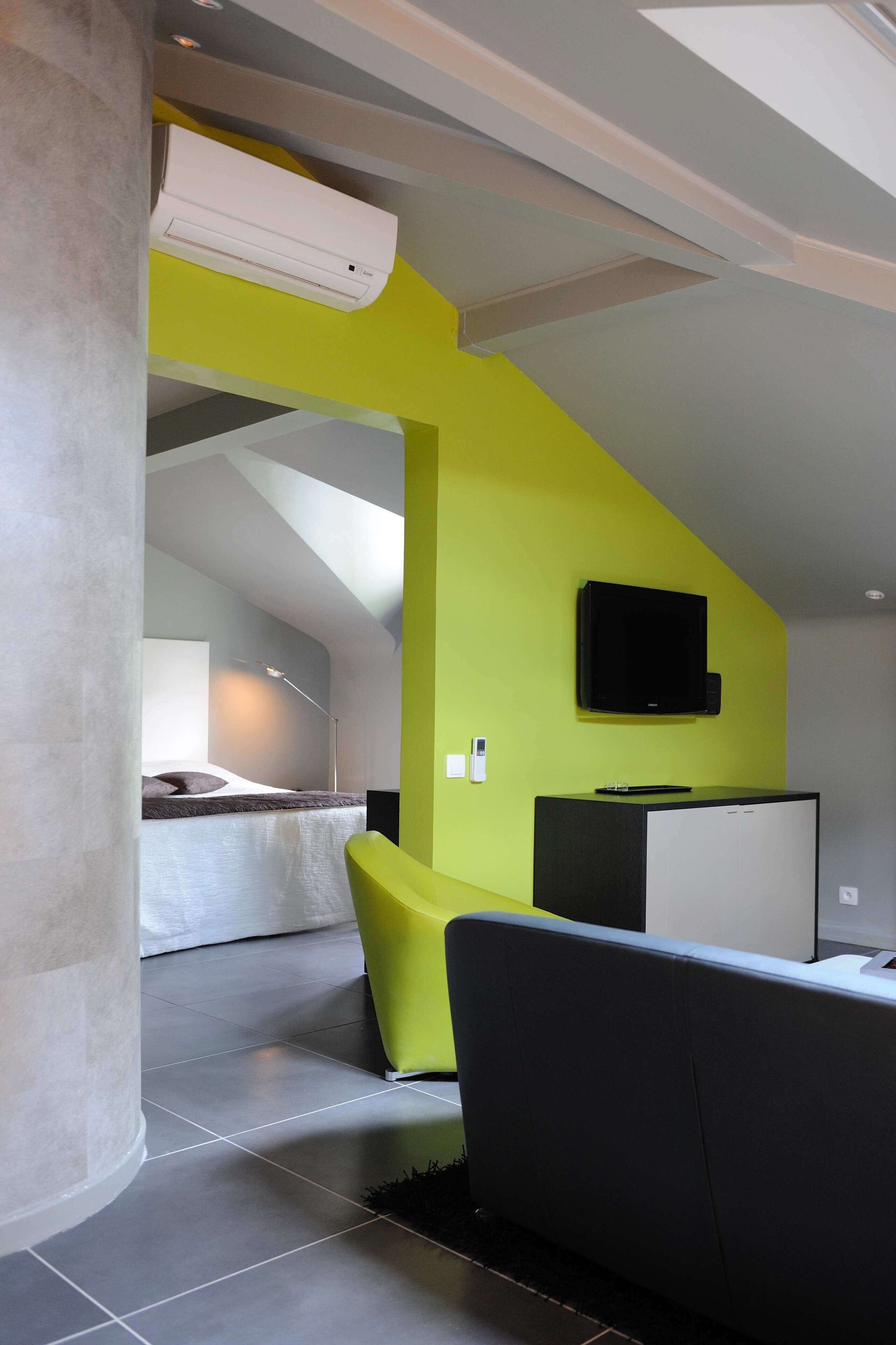 A modern interior with a high ceiling, a built-in air conditioning unit, a flat-screen TV mounted on the wall, and a bed with a headboard in the background.