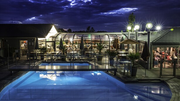 Uma área de piscina com restaurante envidraçado e esplanada.