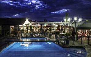 A pool area with a glass-enclosed restaurant and outdoor seating. - Hôtel du Golf (Saint-Etienne)