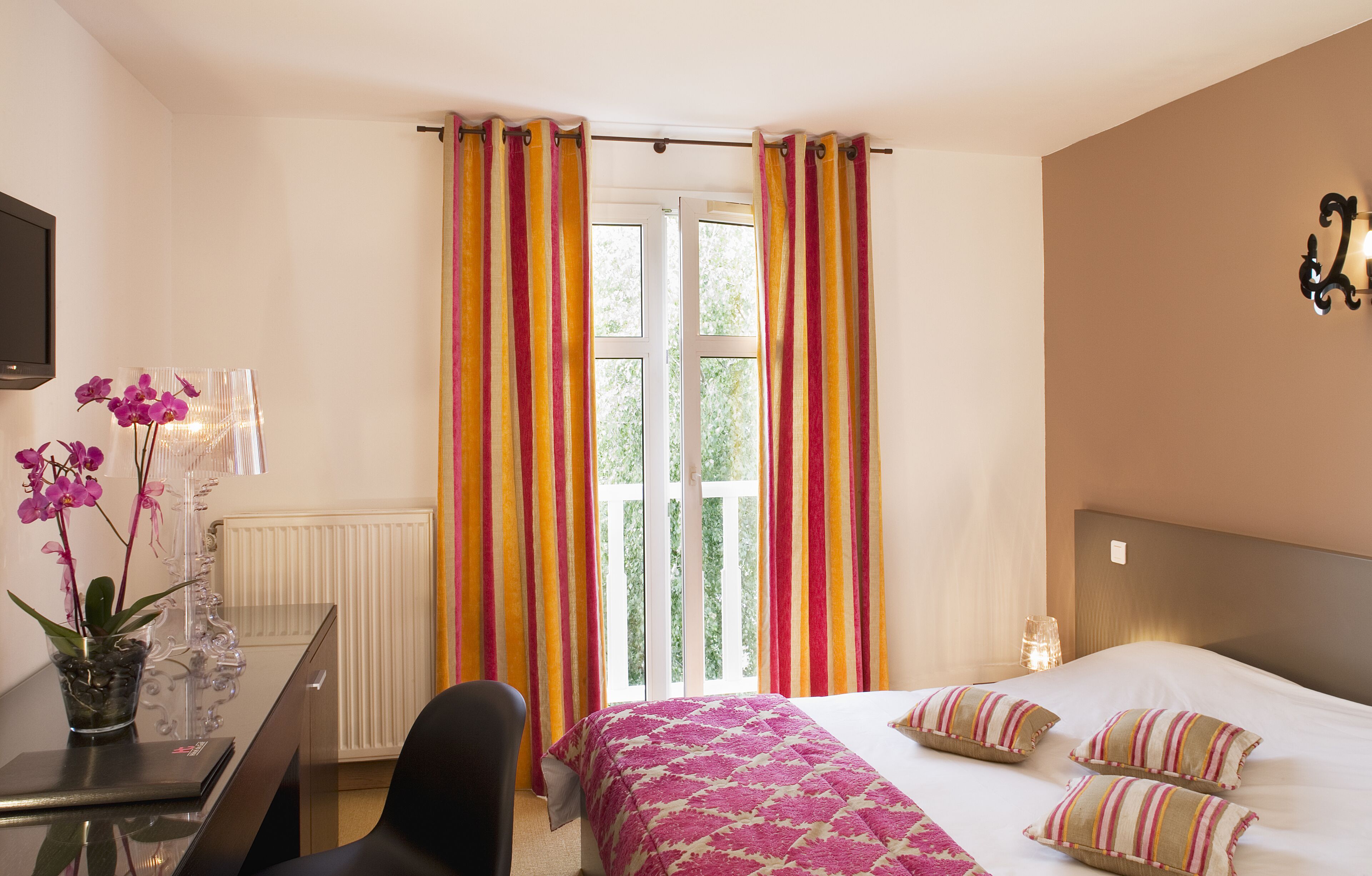 A hotel room with a bed, a desk, a chair, a TV, and a window with curtains.