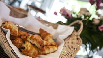 Een mand croissants op een tafel, met een bloemstuk op de achtergrond.