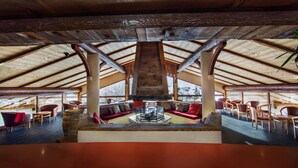 A spacious lounge area with a high ceiling and wooden beams, featuring comfortable seating and a central fire pit. - Alpen Roc (La Clusaz)