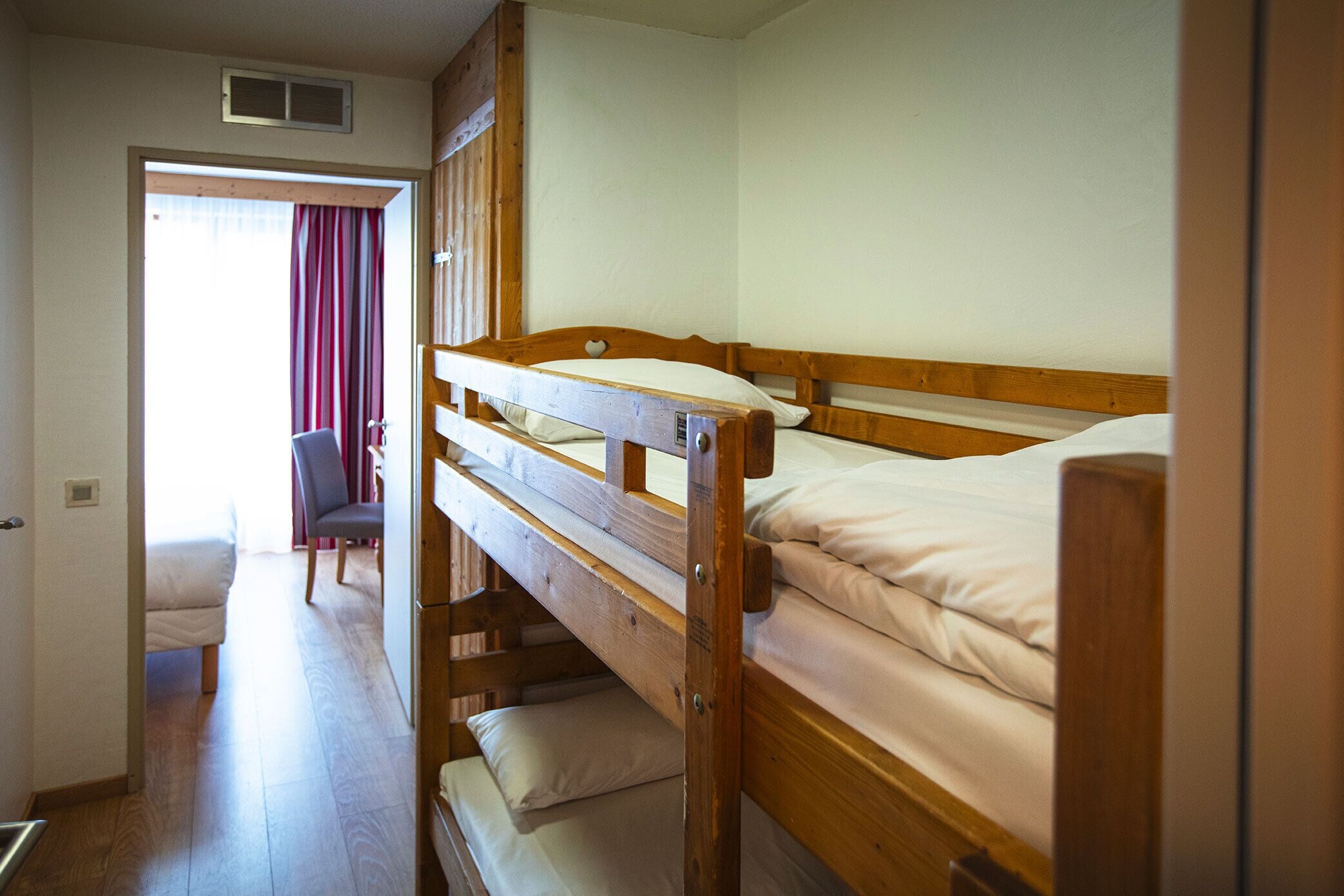 Een slaapkamer met een stapelbed, een houten hoofdbord, een stoel en een deur naar een andere kamer.