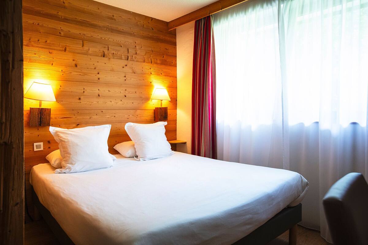 A neatly made bed with white linens and pillows, two bedside lamps, and a wooden headboard.