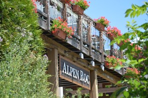 A wooden balcony with flower boxes and a sign that reads "ALPEN ROC".