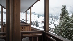 A wooden balcony with a view of a snow-covered village and mountains. - Alpen Roc (La Clusaz)
