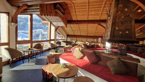 A spacious lounge with a red sofa, multiple seating areas, and large windows offering a view of a snowy landscape. - Alpen Roc (La Clusaz)