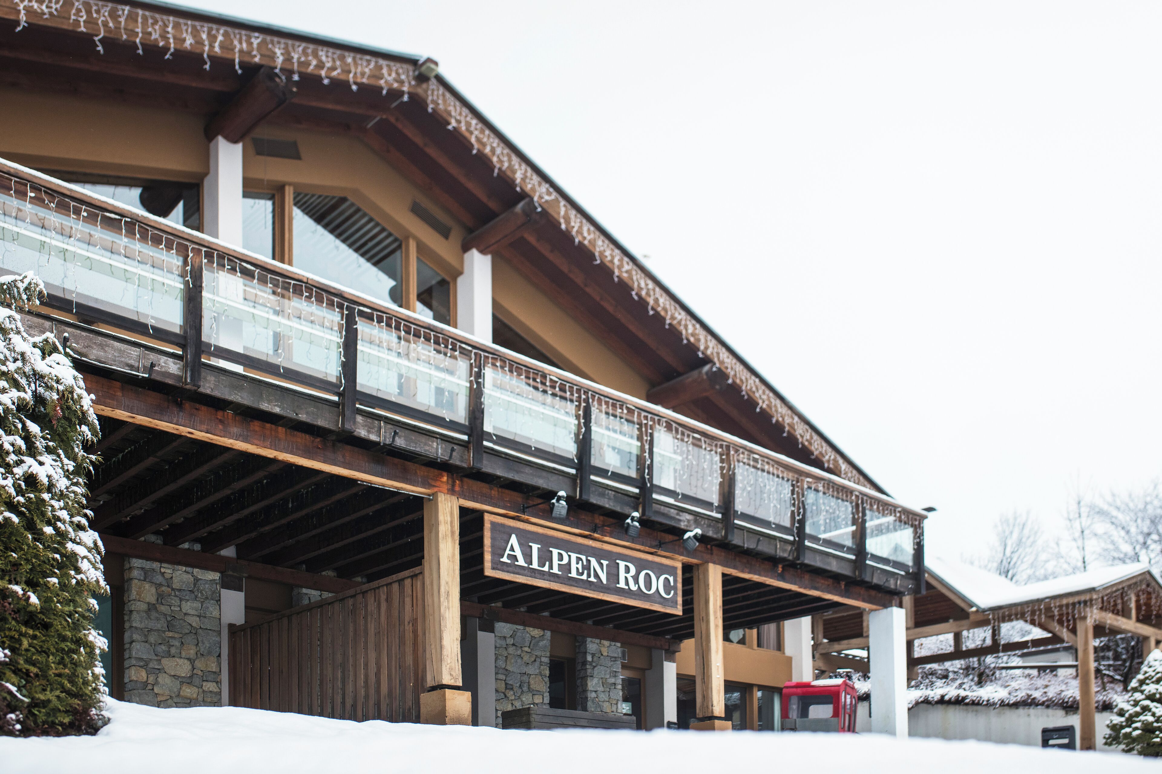 A hotel with a wooden facade, stone pillars, and a sign reading "ALPEN ROC".