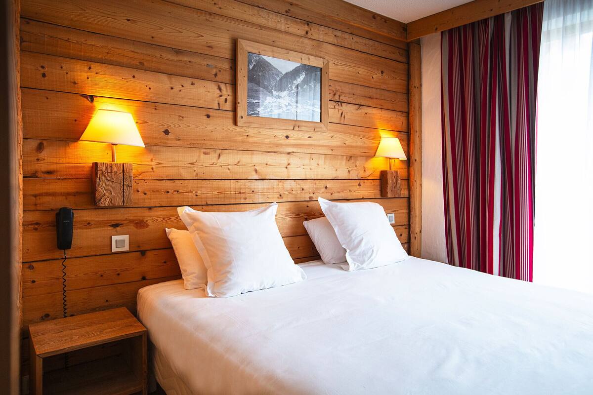 A wooden-paneled room with a bed, two bedside lamps, a telephone, and a framed picture on the wall.