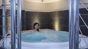 A person in a hot tub with metal railings, surrounded by dark tiled walls. - Alpen Roc (La Clusaz)