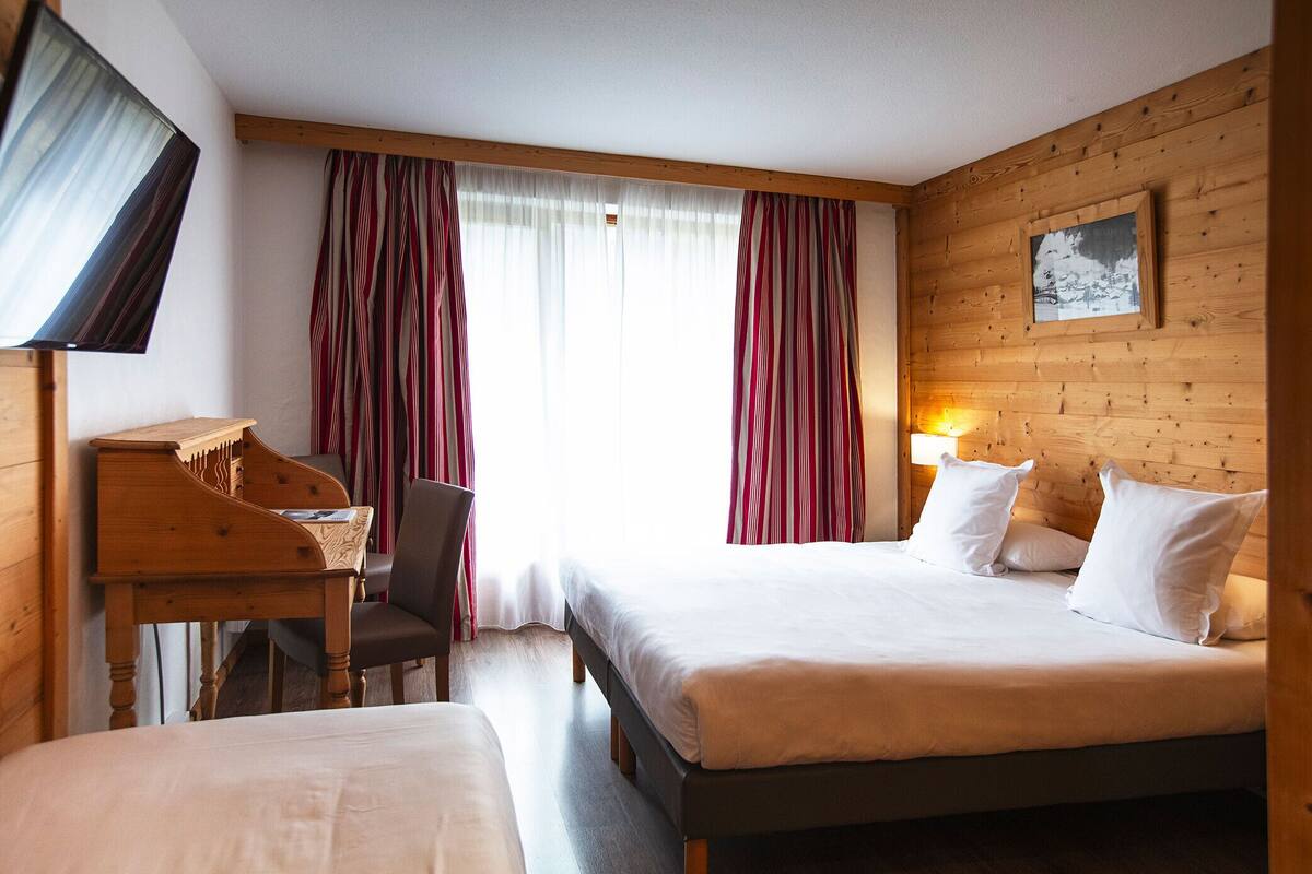 A hotel room with a bed, a desk, a chair, a TV, and a window with curtains.