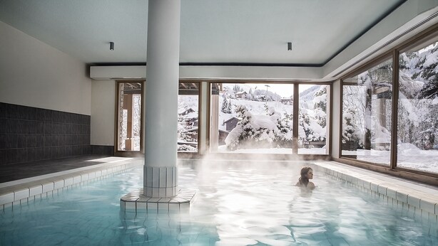 An indoor swimming pool with a view of snowy mountains through large windows. - Alpen Roc (La Clusaz)