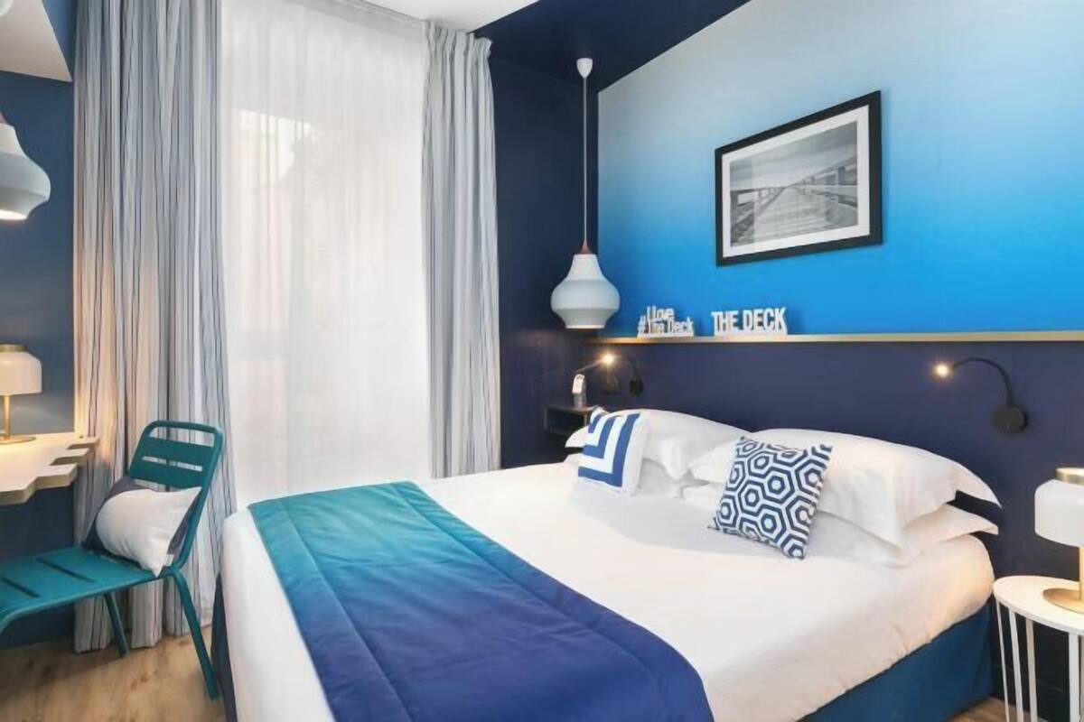 A hotel room with a bed, a chair, a desk, a lamp, and a picture on the wall.