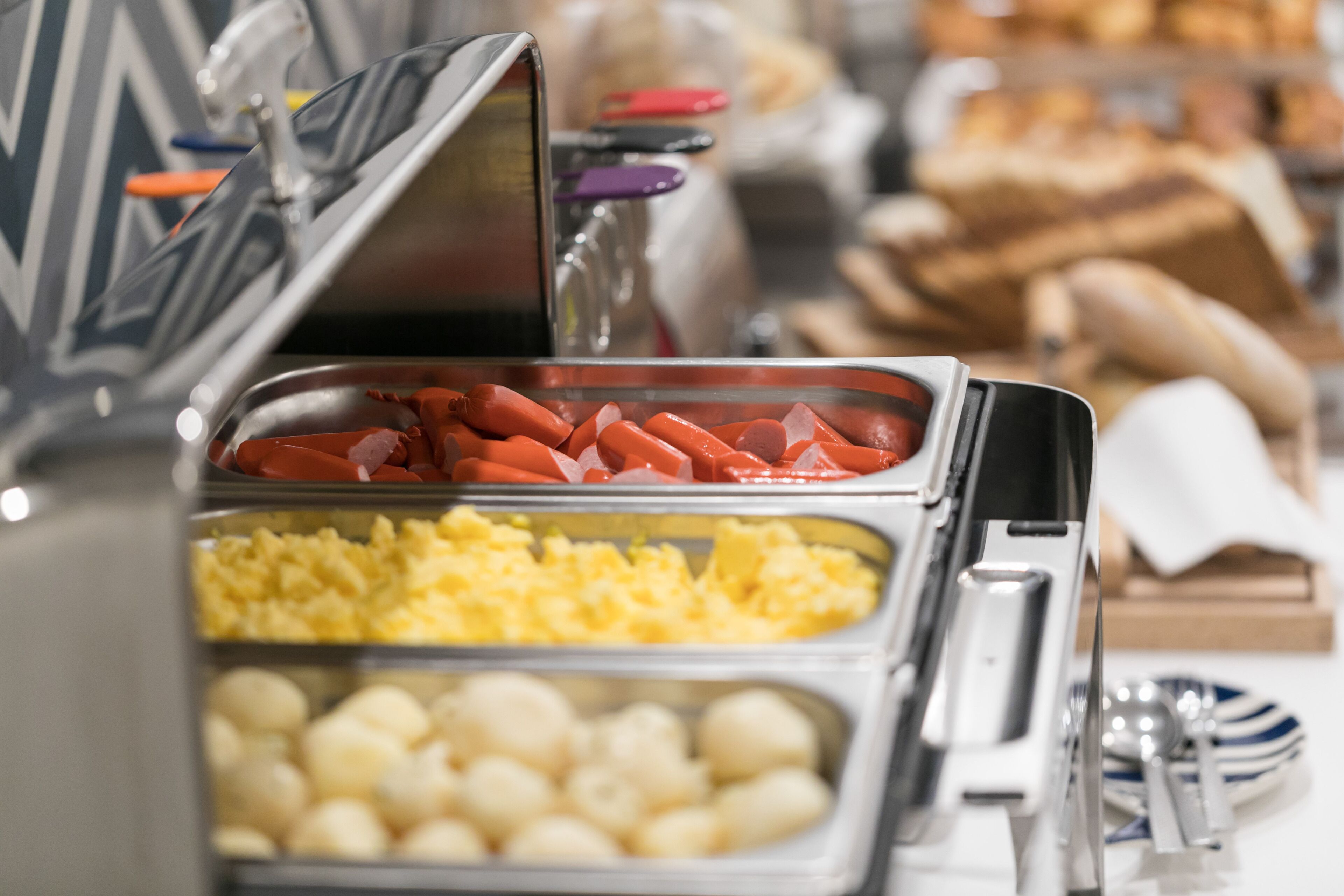 Un bufé con diferentes opciones de comida, como salchichas, huevos revueltos y papas.