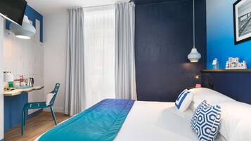 A hotel room with a bed, a desk with a chair, a TV, and a window with curtains.