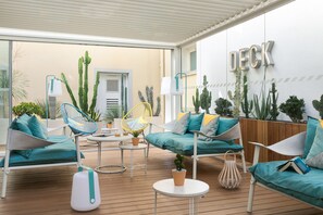 A sunlit outdoor deck with seating areas, potted plants, and a 'DECK' sign. - The Deck Hotel by HappyCulture (Nice)