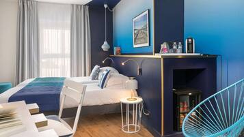 A modern bedroom with a bed, bedside table, lamp, chair, and a small shelf with items.