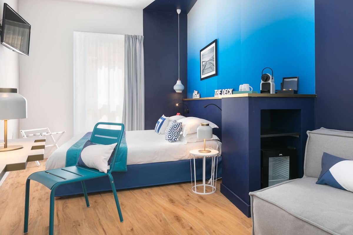 A modern bedroom with a bed, a chair, a small table, a fireplace, and a TV mounted on the wall.